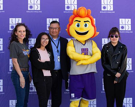 Mascot with President Pendergrass and naming contest winners with SJC purple background.